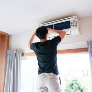 HVAC expert adjusting an AC unit that is mounted above a window.